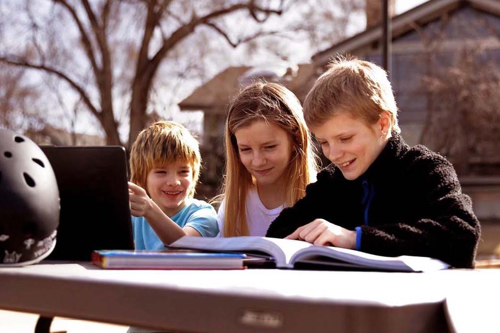 三个学生坐在外面的桌子旁用笔记本电脑学习