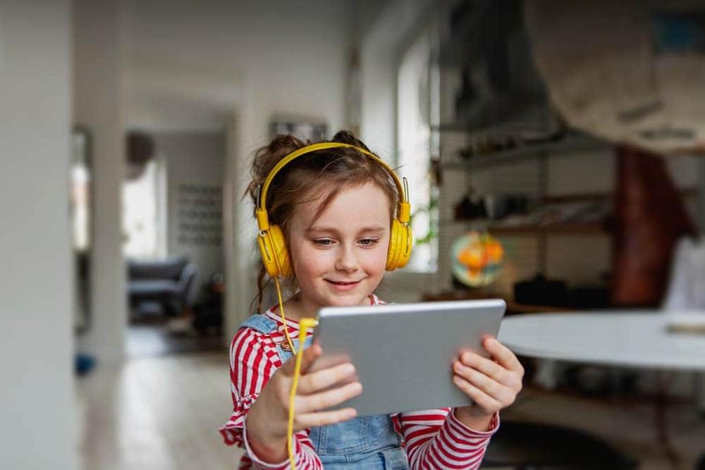 戴着黄色耳机的年轻女学生微笑着看着笔记本电脑，在爱荷华连接学院上在线课程.