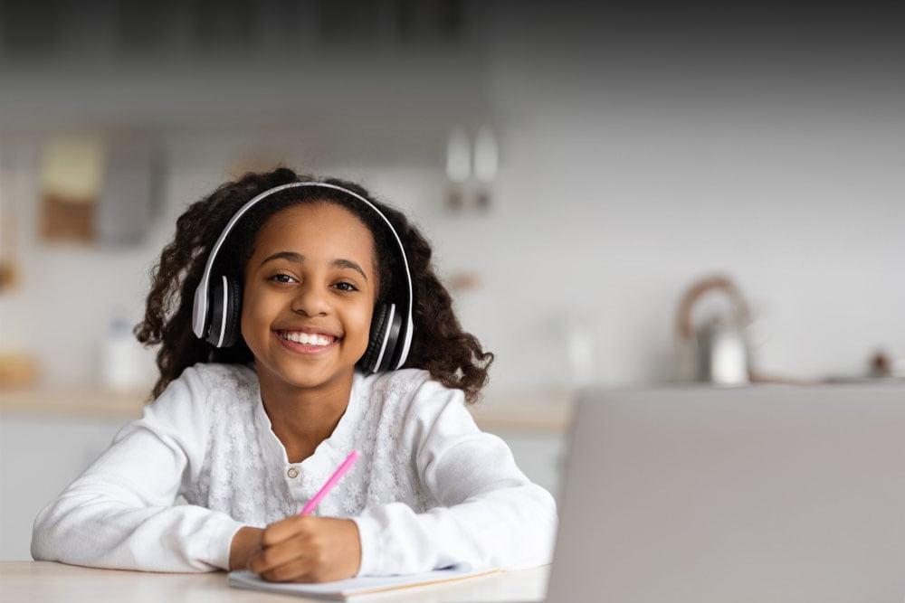 在密苏里连接学院上在线课程时，一个穿着白衬衫的小女孩对着电脑微笑. 