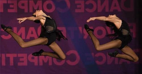 Two young girls dance on a stage in black leotards. 